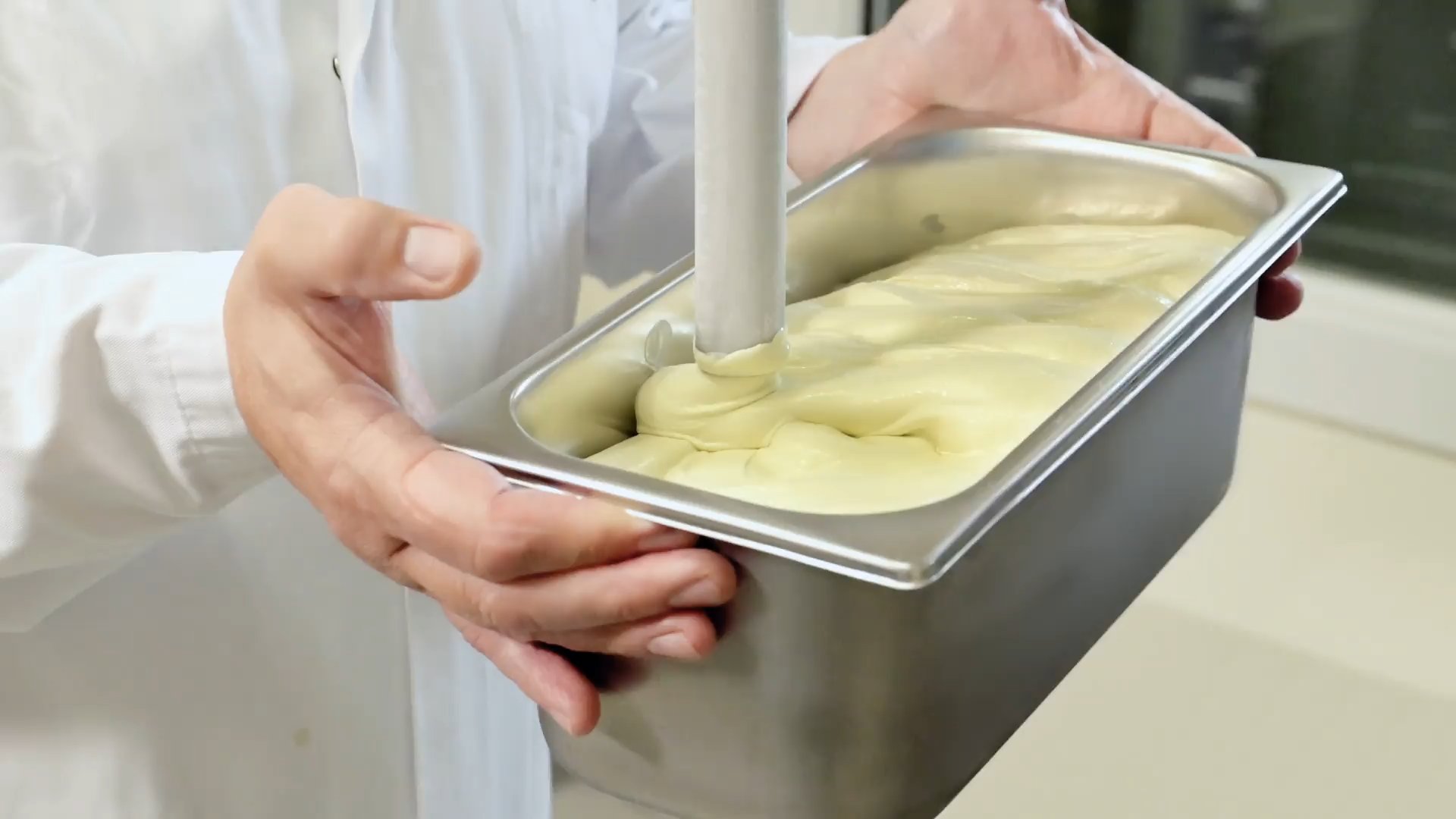 Frisch zubereitetes Eis läuft aus der Eismaschine in eine Edelstahlwanne